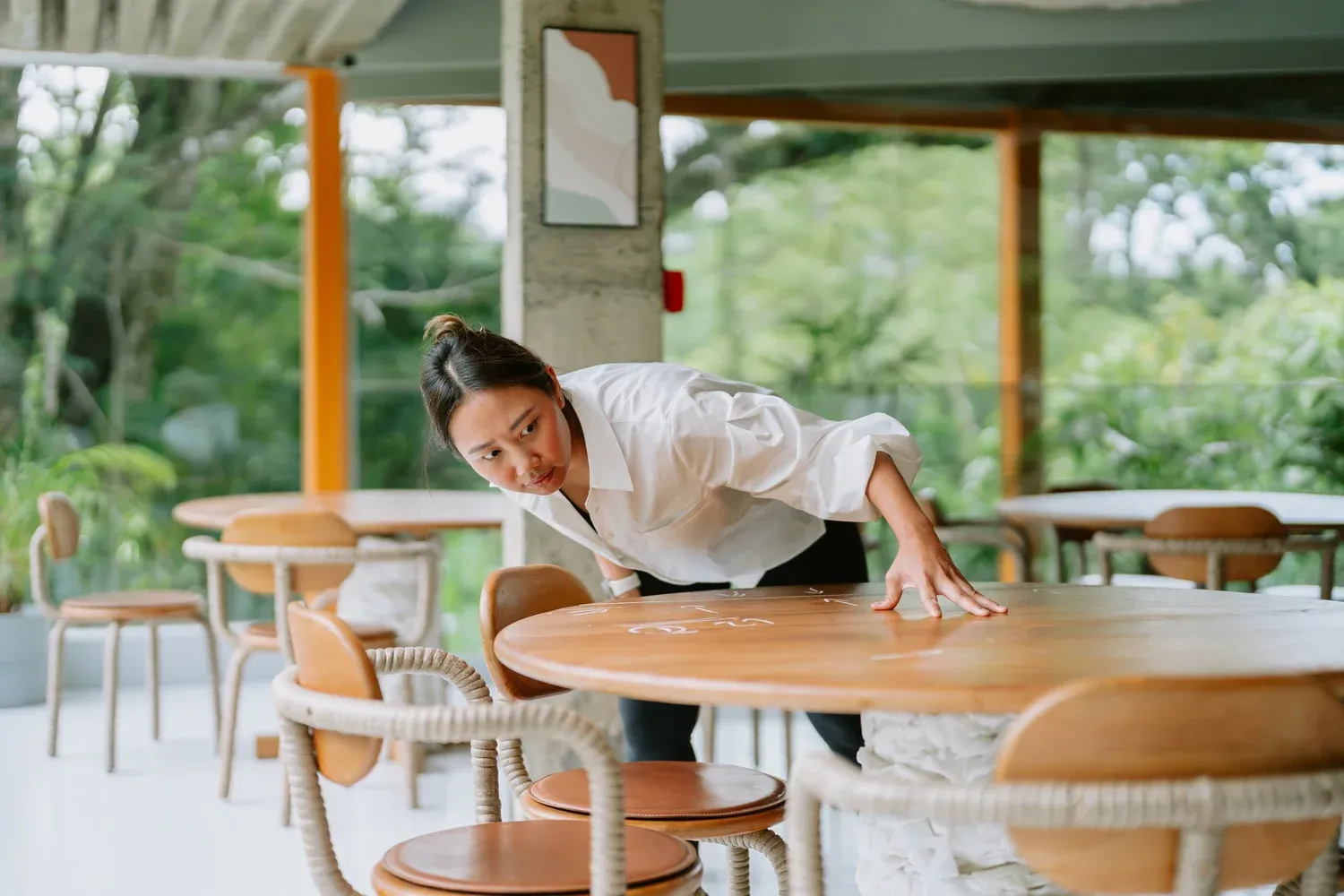 A woman examining a wooden table in a light-filled interior
