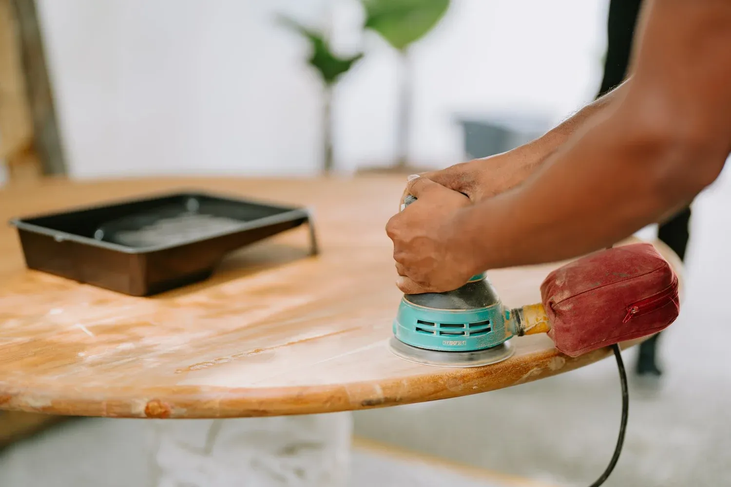 Hands guiding an orbital sander across a wooden tabletop